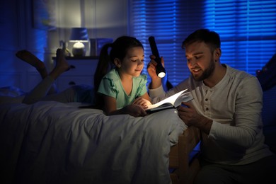 Photo of Father with little daughter reading fairy tale in dark bedroom