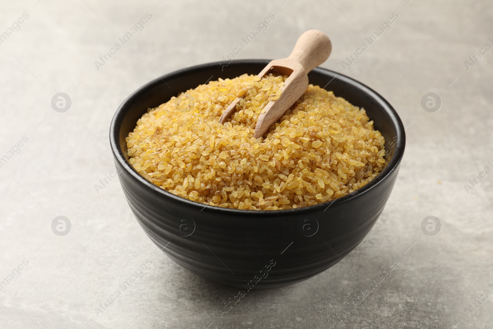 Photo of Bowl and scoop with raw bulgur on gray table, closeup