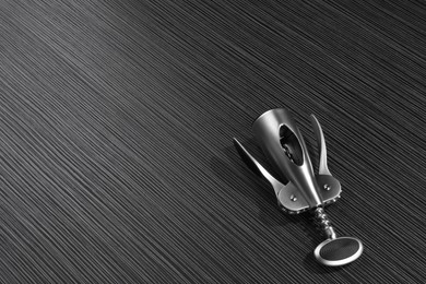 Photo of One wing corkscrew on black wooden table. Space for text