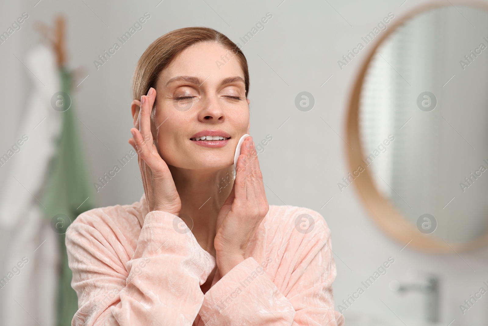 Photo of Beautiful woman removing makeup with cotton pad indoors, space for text