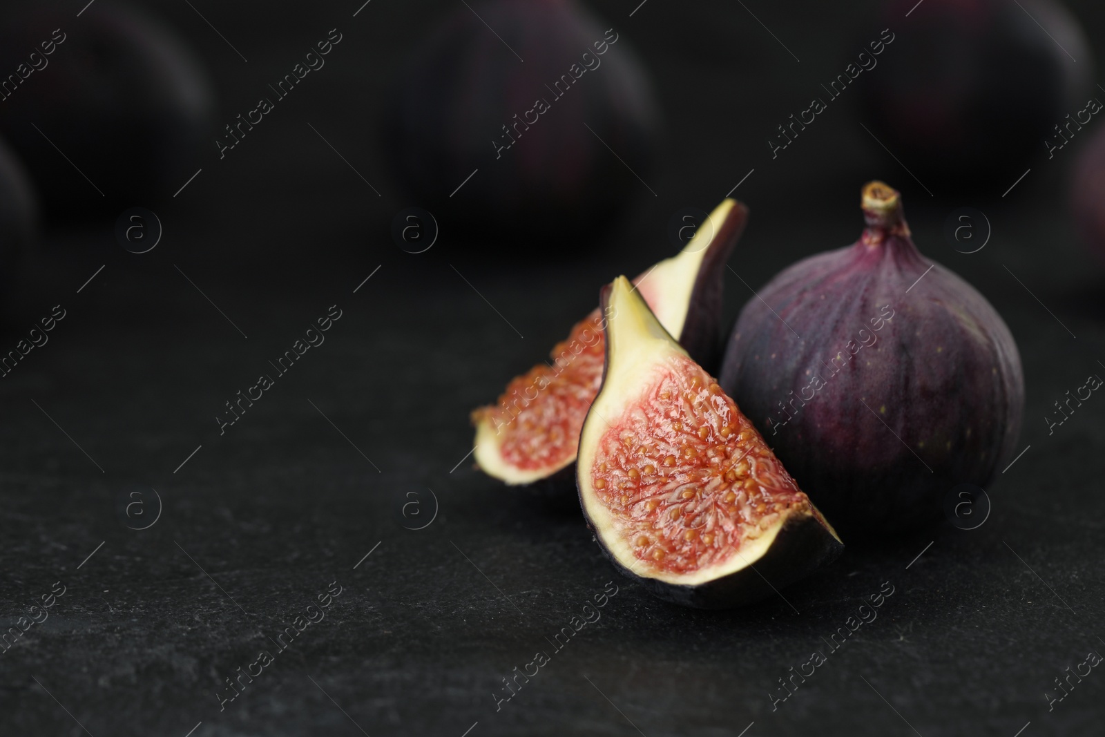 Photo of Tasty raw figs on black slate table, closeup. Space for text