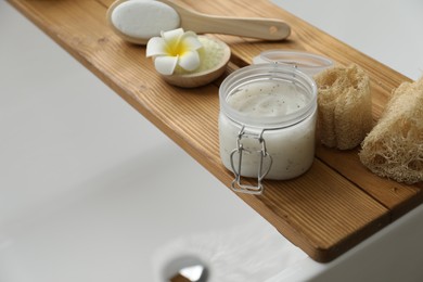 Wooden tray with spa products and plumeria flower on bath tub, closeup