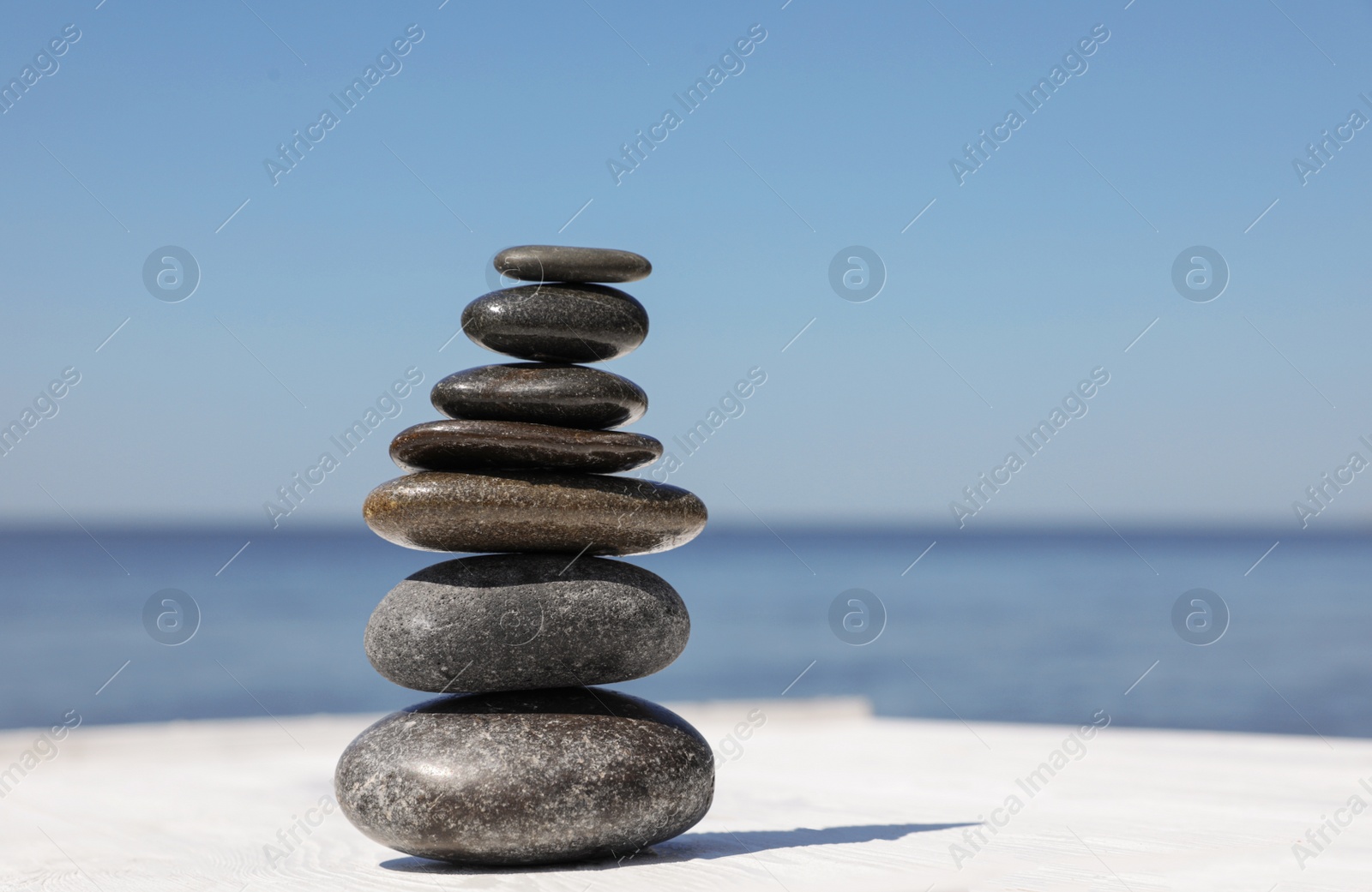 Photo of Stack of stones on wooden pier near sea, space for text. Zen concept