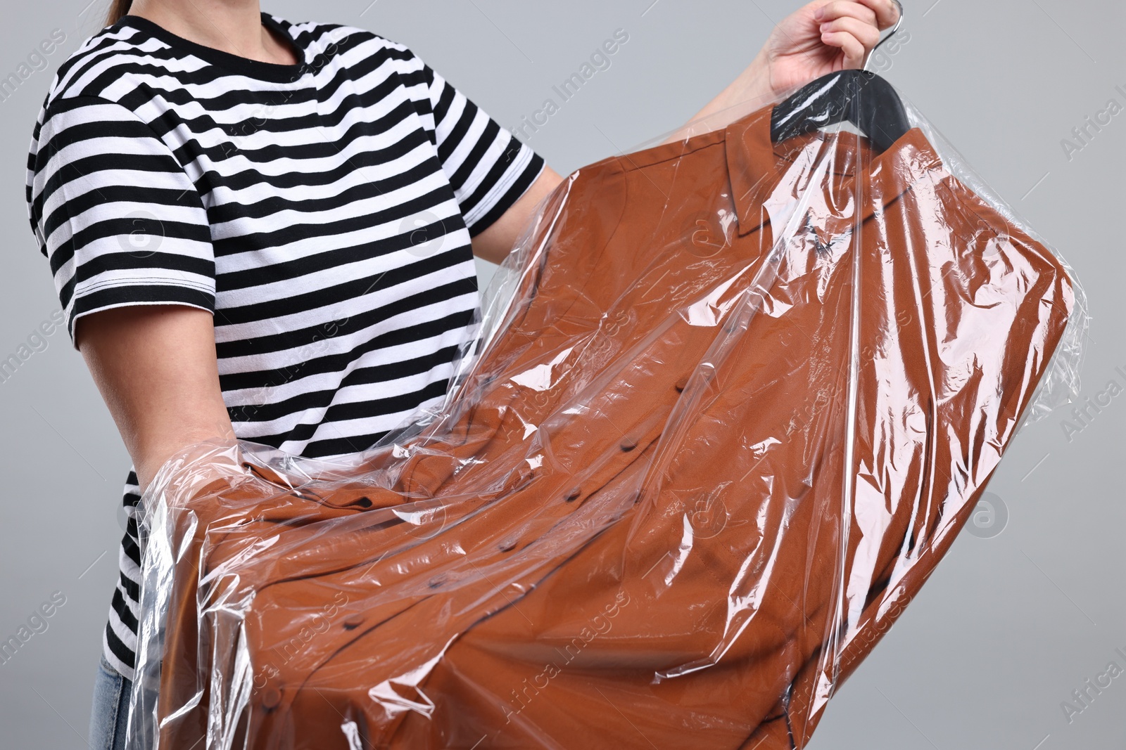 Photo of Dry-cleaning service. Woman holding shirt in plastic bag on gray background, closeup