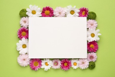 Photo of Frame made of beautiful chrysanthemum flowers and blank card on green background, flat lay. Space for text