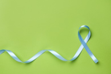 Photo of Light blue awareness ribbon on green background, top view. Space for text