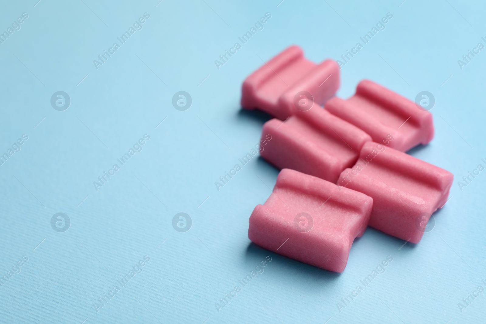 Photo of Tasty pink chewing gums on light blue background, space for text