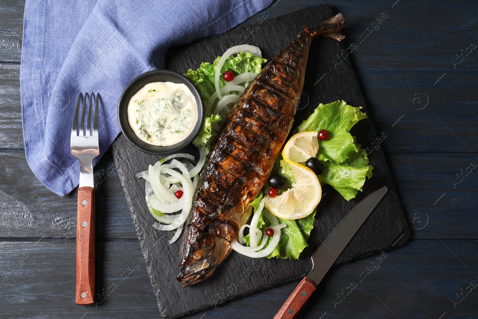 Photo of Slate plate with delicious grilled fish and sauce on wooden table, top view