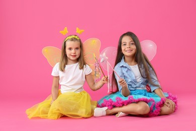 Photo of Cute little girls in fairy costumes with wings and magic wands on pink background