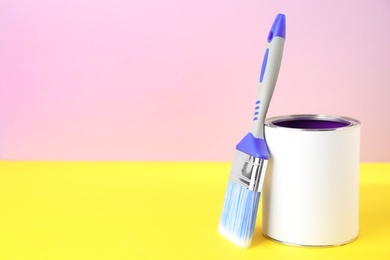Photo of Blank can of paint with brush on table against color background. Space for text