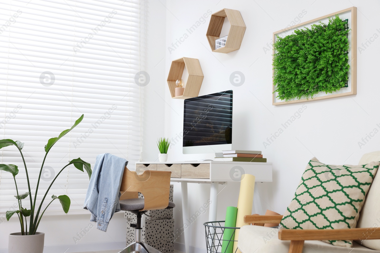 Photo of Green artificial plant wall panel and desk with computer in light room. Interior design