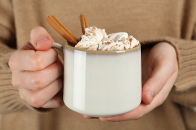 Photo of Woman holding cup of delicious hot chocolate with marshmallows and cinnamon sticks, closeup