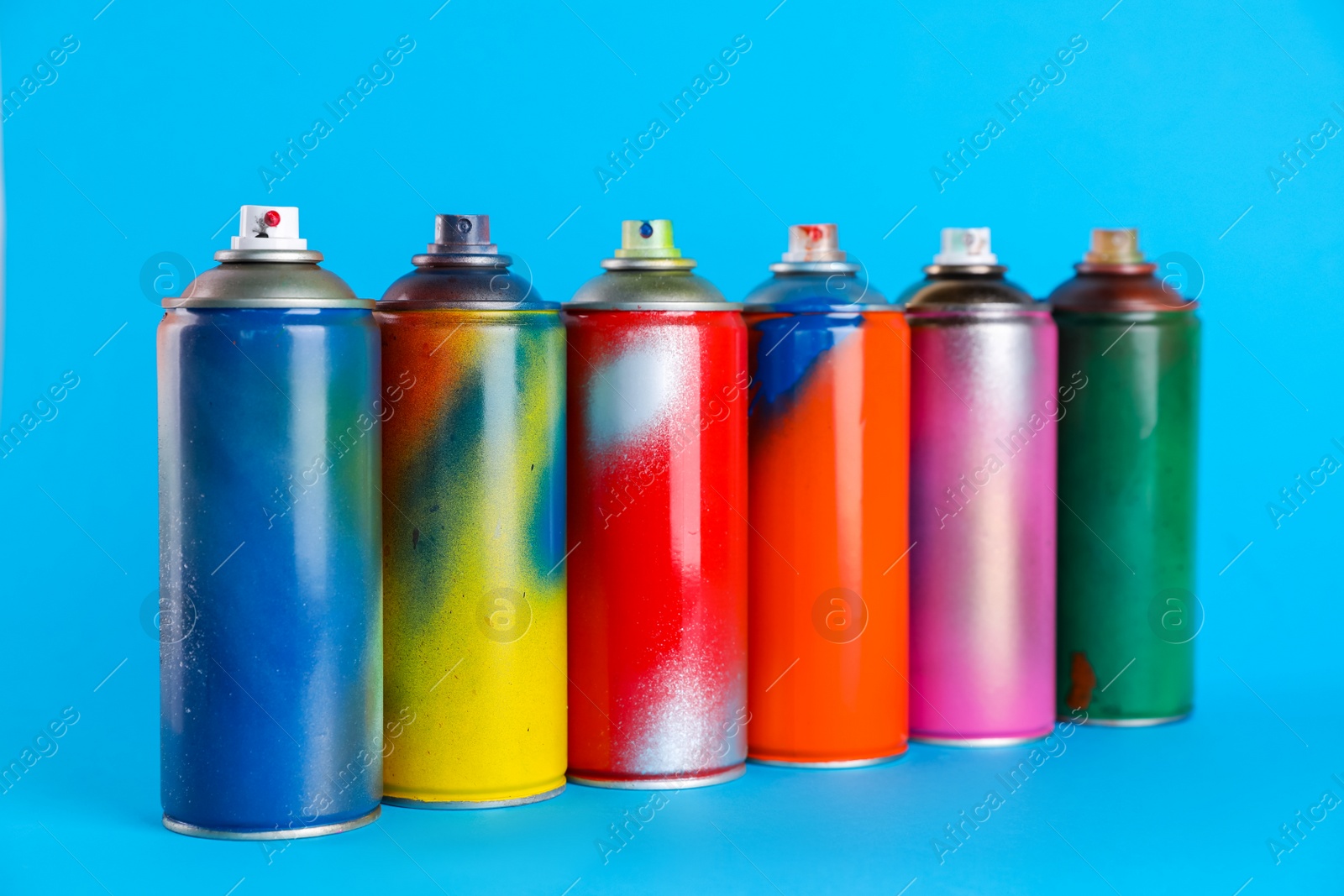 Photo of Used cans of spray paints on light blue background