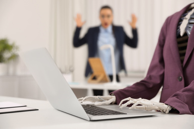 Photo of Human skeleton in suit using laptop at table in office, closeup