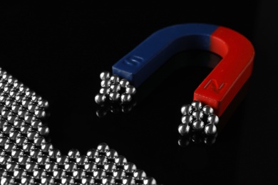 Photo of Magnet attracting chrome balls on black background. Business leadership concept
