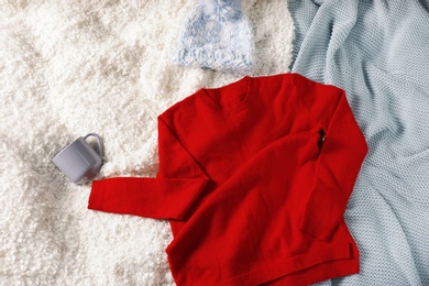 Flat lay composition with red sweater and hat on soft blankets