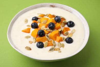 Photo of Bowl of delicious semolina pudding with blueberries, pumpkin and seeds on green background, closeup