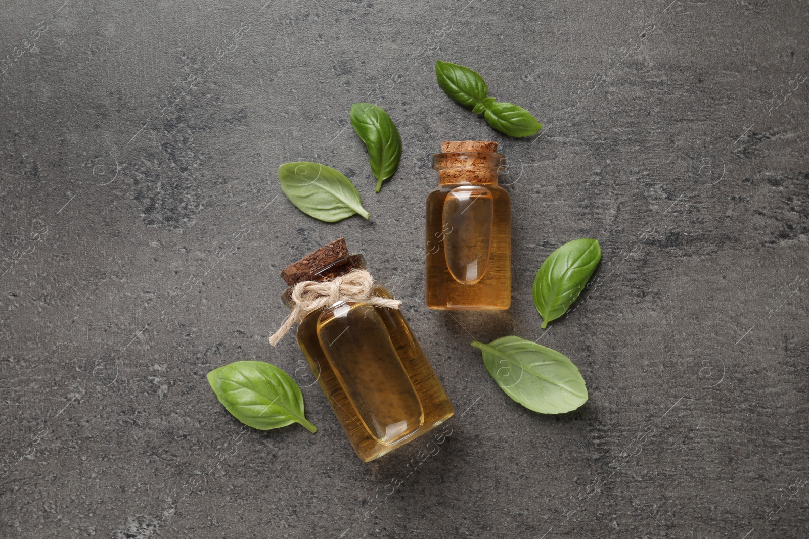 Photo of Bottles of essential basil oil and fresh leaves on grey table, flat lay