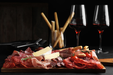 Photo of Tasty prosciutto with other delicacies served on black table