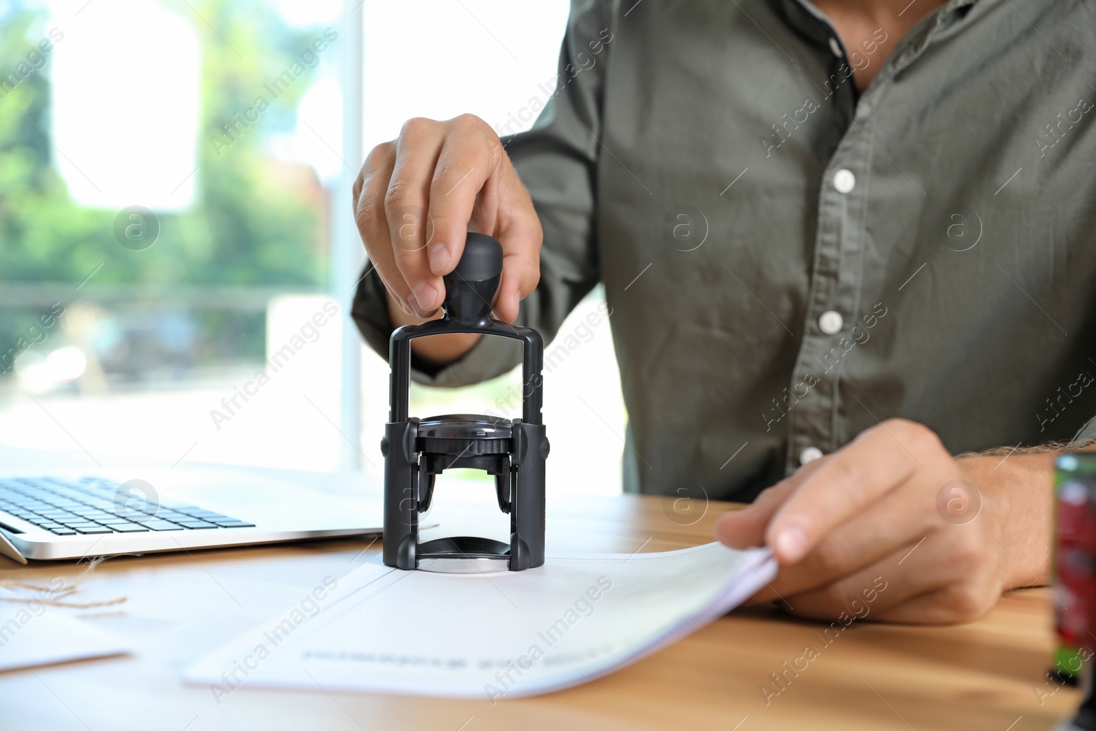 Photo of Male notary stamping document at table in office, closeup