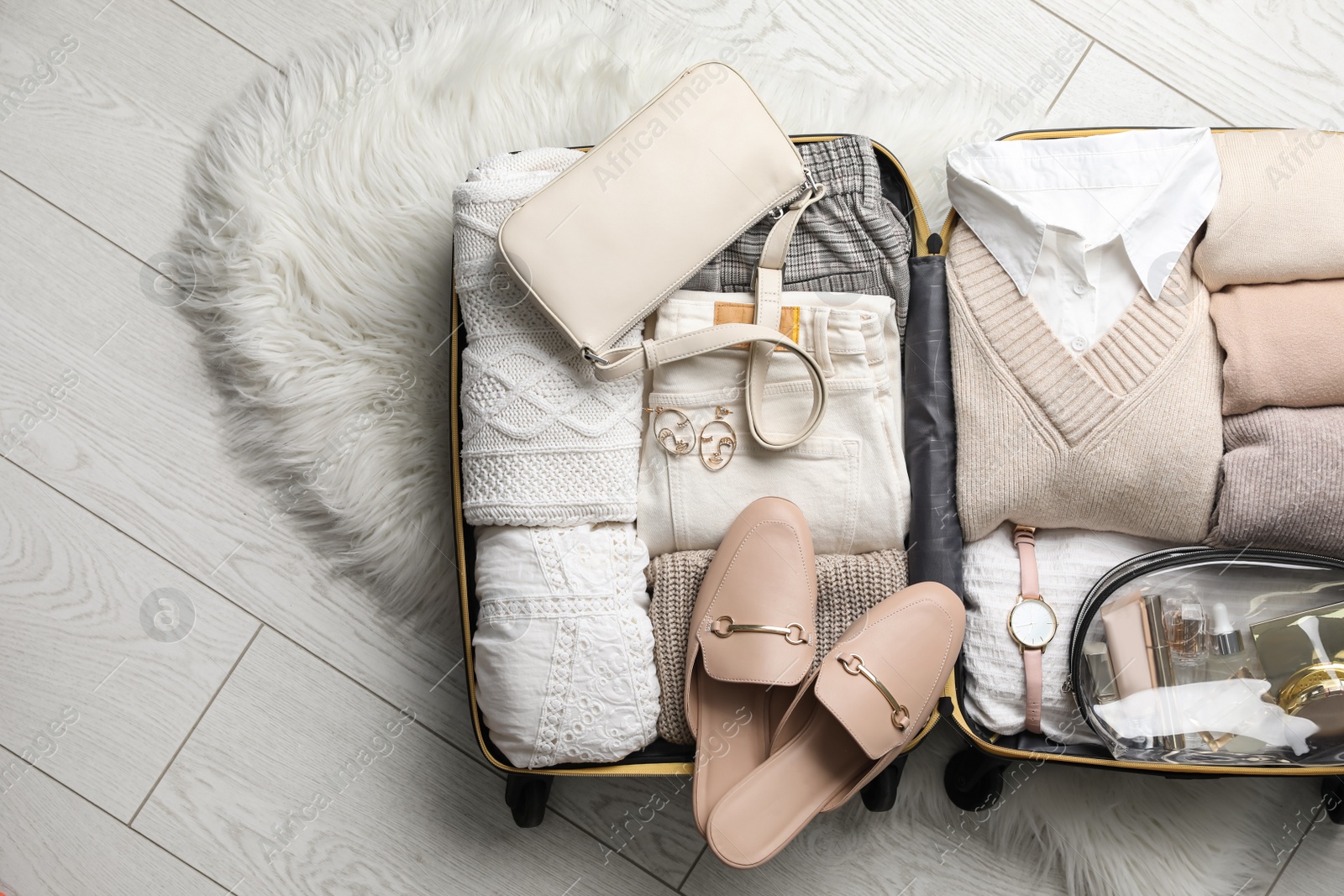 Photo of Open suitcase with folded clothes, shoes and accessories on floor, top view