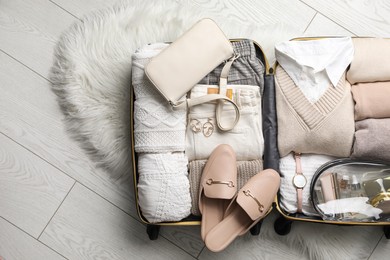 Open suitcase with folded clothes, shoes and accessories on floor, top view