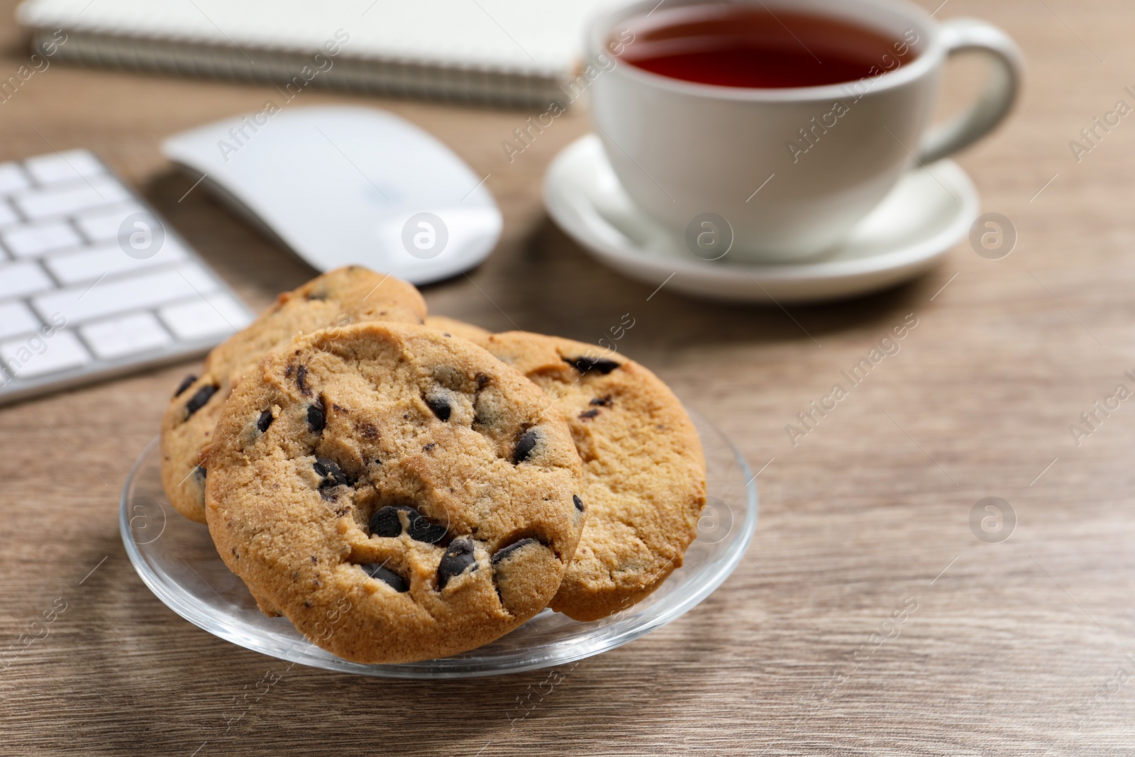 Photo of Chocolate chip cookies on wooden table at workplace, closeup