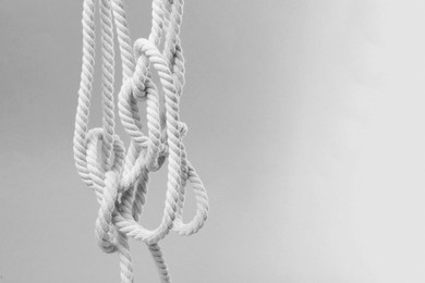 Hemp rope with knot hanging on light grey background, space for text