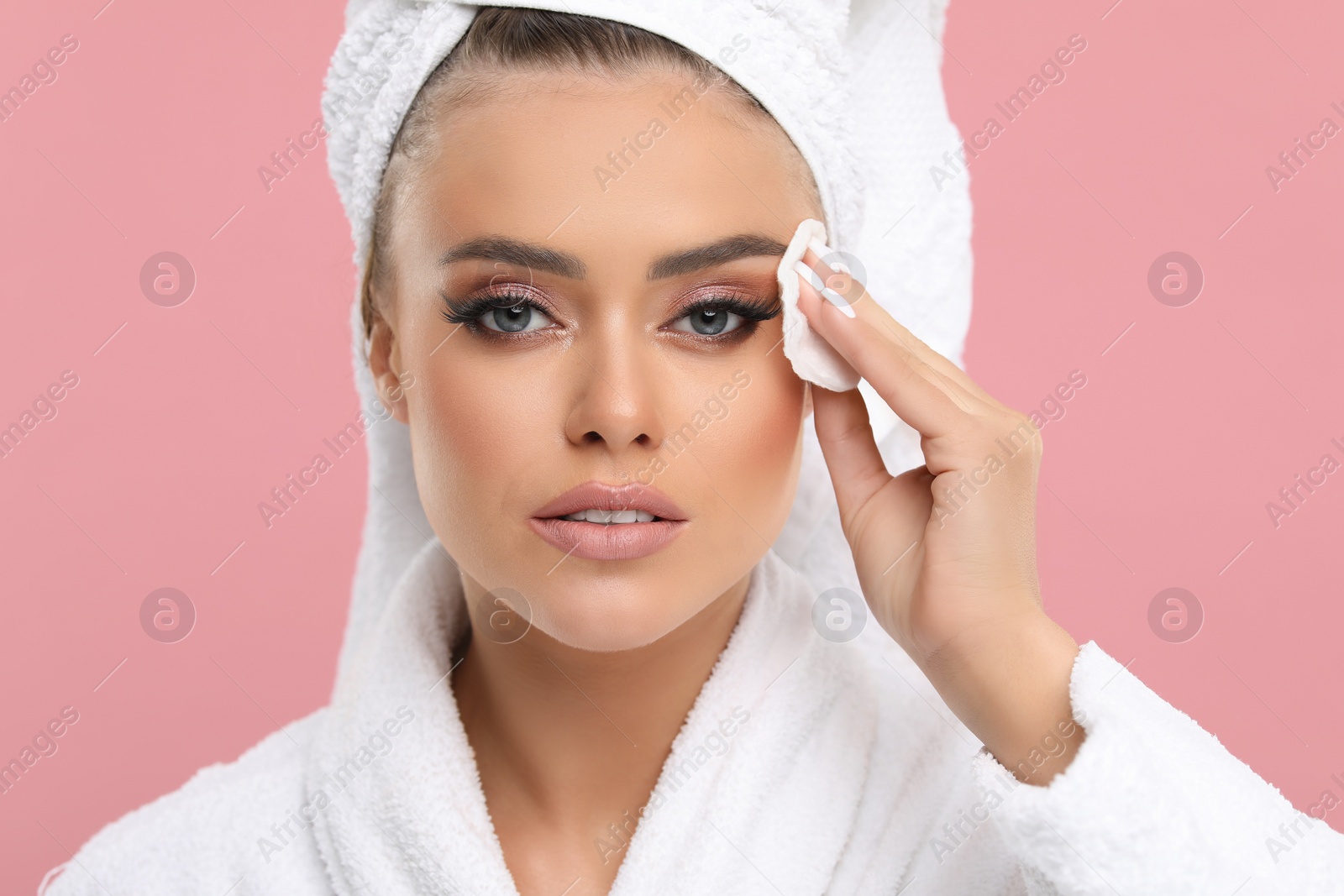 Photo of Beautiful woman removing makeup with cotton pad on pink background