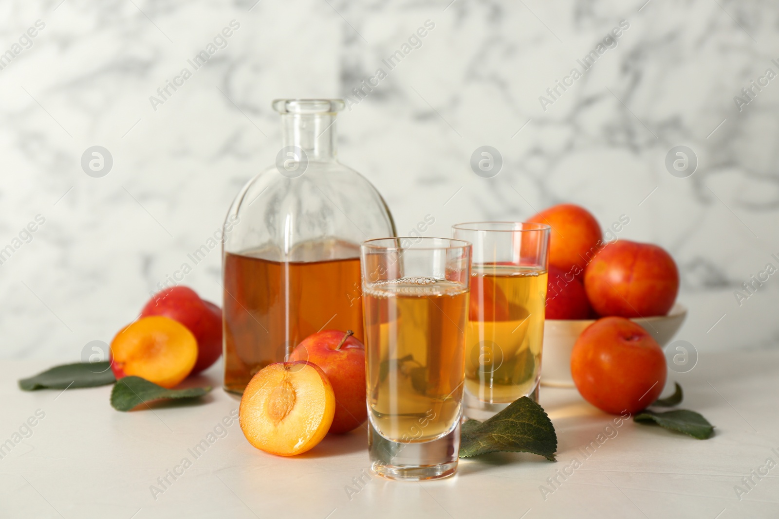 Photo of Delicious plum liquor and ripe fruits on white table. Homemade strong alcoholic beverage