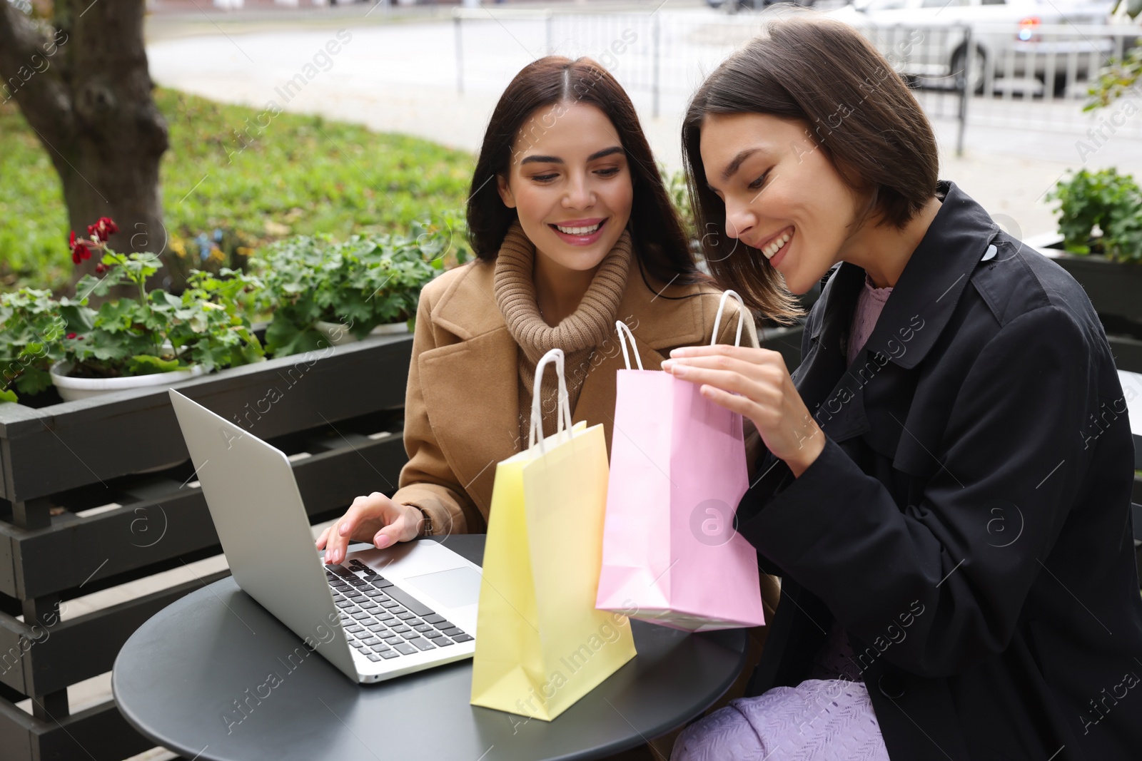 Photo of Special Promotion. Happy young women with shopping bags using laptop in outdoor cafe