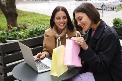 Photo of Special Promotion. Happy young women with shopping bags using laptop in outdoor cafe