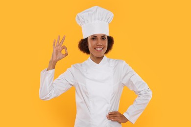 Photo of Happy female chef in uniform showing ok gesture on orange background