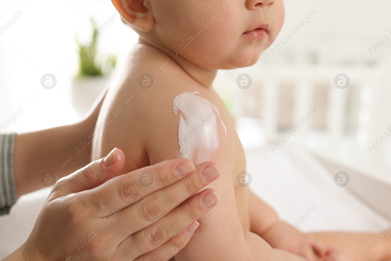 Photo of Mother applying body cream on her little baby at home, closeup