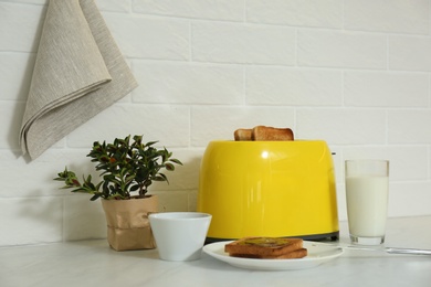 Modern toaster with bread slices, glass of milk and plant on white table in kitchen