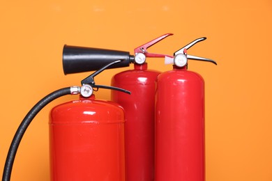 Three red fire extinguishers on orange background, closeup