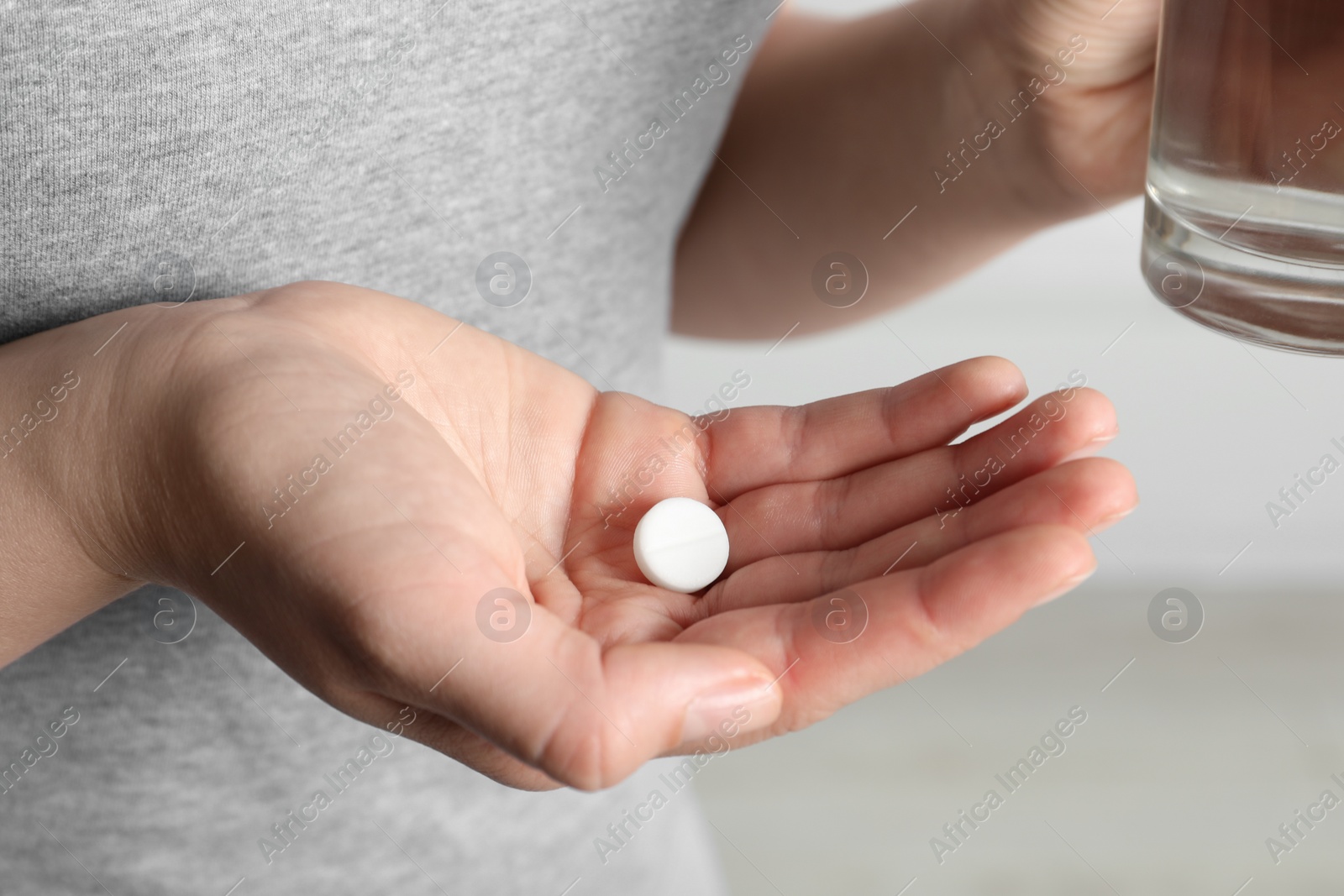 Photo of Woman with pill and glass of water on blurred background, closeup