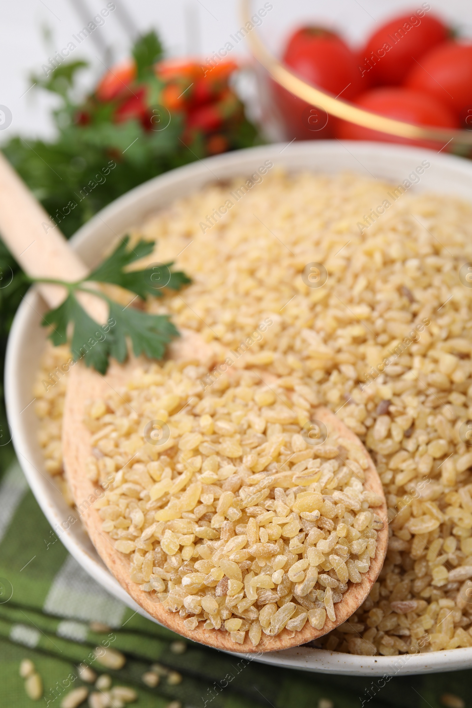 Photo of Bowl and spoon with raw bulgur on table, closeup