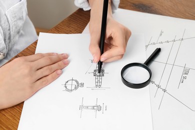 Jeweler drawing sketch of elegant ring on paper at wooden table, closeup