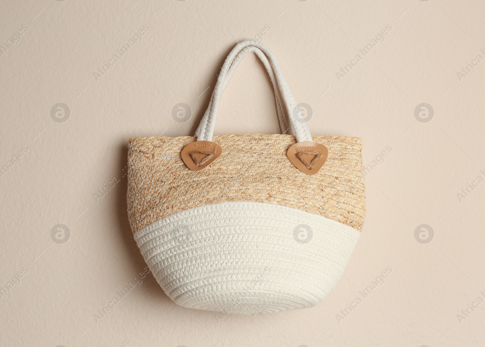 Photo of Elegant woman's straw bag hanging on beige background