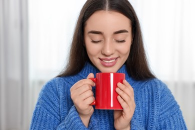 Happy young woman holding red ceramic mug at home