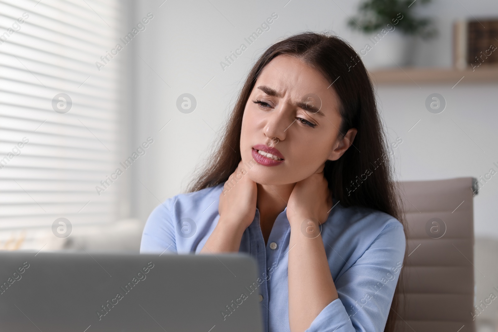 Photo of Young woman suffering from neck pain in office