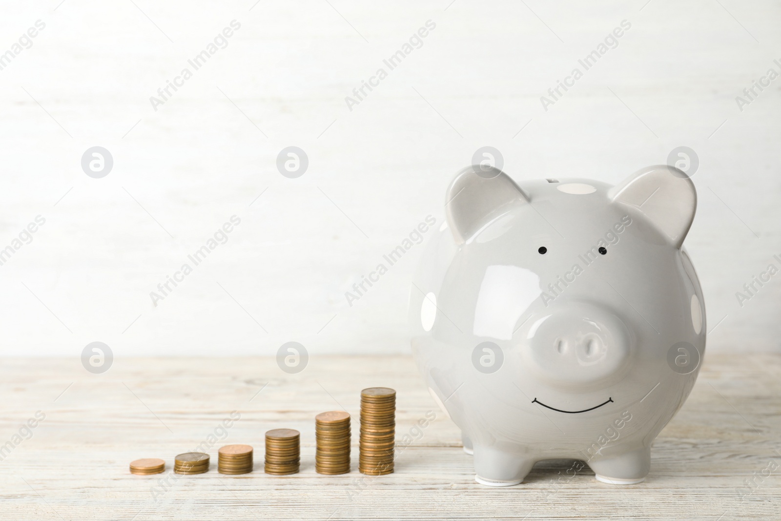Photo of Ceramic piggy bank and many coins on table against light background. Space for text