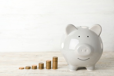 Ceramic piggy bank and many coins on table against light background. Space for text