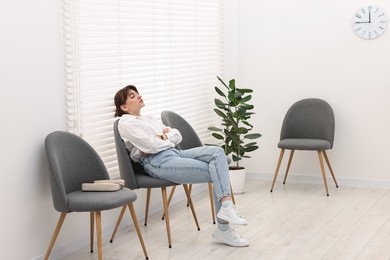 Tired woman sitting on chair and waiting for appointment indoors