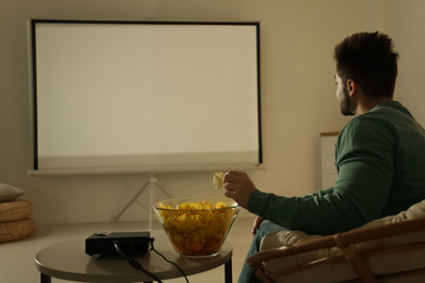 Young man watching movie using video projector at home