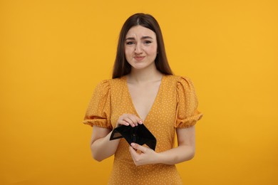 Photo of Sad woman showing empty wallet on orange background