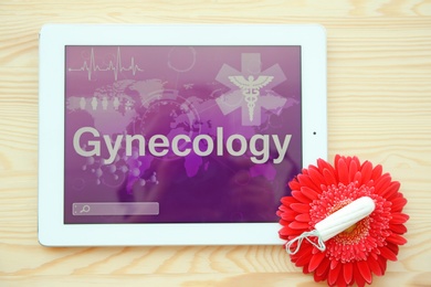 Photo of Flat lay composition with tablet, flower and tampon on wooden background. Gynecological checkup