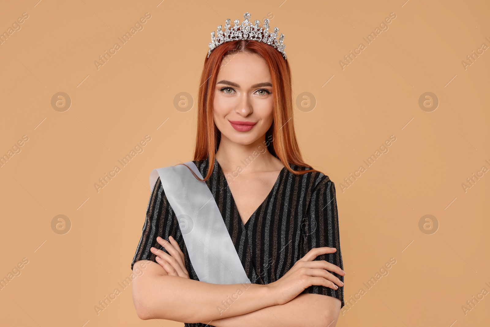 Photo of Beautiful young woman with tiara and ribbon in dress on beige background. Beauty contest