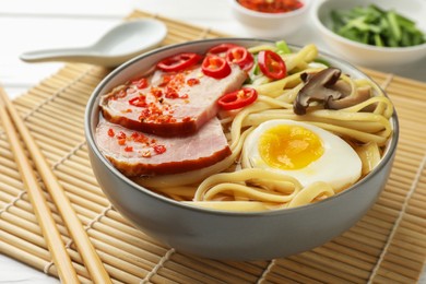 Photo of Delicious ramen in bowl and chopsticks on white table, closeup. Noodle soup